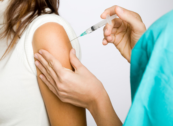 A person receiving a B-12 vitamin shot in their upper arm from a healthcare professional. The healthcare worker is wearing gloves and using a syringe while the recipient appears calm and relaxed.