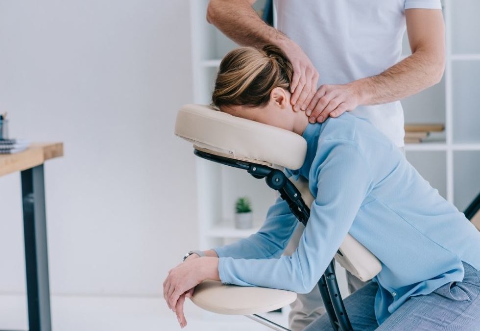 Person receiving a seated chair massage from a massage therapist, with head resting on a padded support and back exposed for treatment in a calm, professional setting.