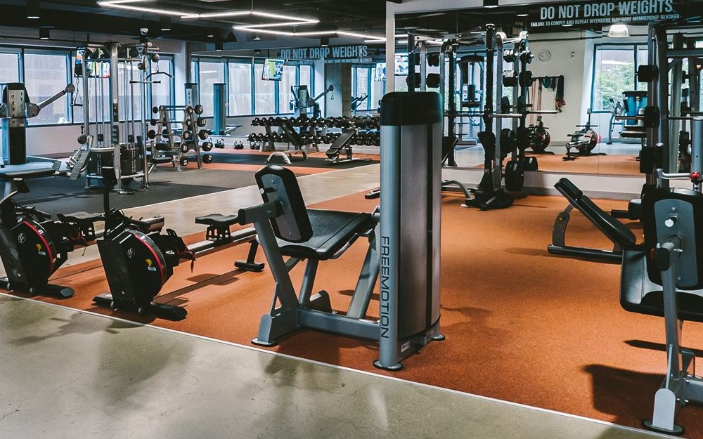 Interior view of a gym with multiple benches and cable machines. The space is well-lit, with a clean, modern design. The benches are arranged in a neat row, and the cable machines are strategically placed, offering a variety of strength training options. Fitness equipment is visible throughout the space, with a focus on functionality and comfort.